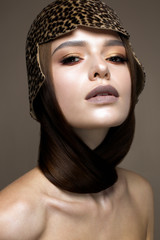 A young girl in a hat in the form of a helmet with a leopard coloring. A beautiful model with straight long hair and gentle make-up in chocolate shades. Beauty of the face. Photo taken in the studio.