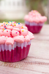 Red velvet cupcake decorated with pink cream on wood background. Warm and pastel color tone.