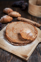 freshly baked sweet pancakes stacked on brown baking paper, croissants and grapes on a dark brown wooden table on a dark gray background