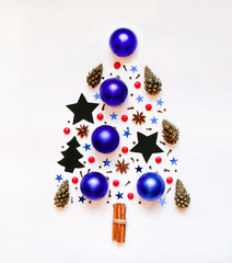 Christmas tree from small objects: stars, blue Christmas decorations, anise, cinnamon, cloves, cones, red candies. On a white background. Top view. christmas, new year