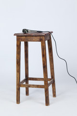 This is a photo of a microphone sitting on top of a wooden stool lite from above. Shot on a white background
