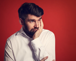 Fototapeta premium Unhappy thinking bearded business man holding the face the hand in white shirt on red background. Closeup toned portrait of stress