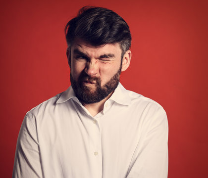 Grimacing emotional disgasted bearded business man looking unhappy in white style shirt. Closeup portrait on red background. Closeup toned portrait