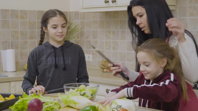 Little girls help mother to cook salad for dinner