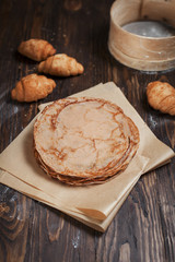 freshly baked sweet pancakes stacked on brown baking paper and croissants on a dark brown wooden table on a dark gray background