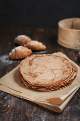 freshly baked sweet pancakes stacked on brown baking paper and croissants on a dark brown wooden table on a dark gray background