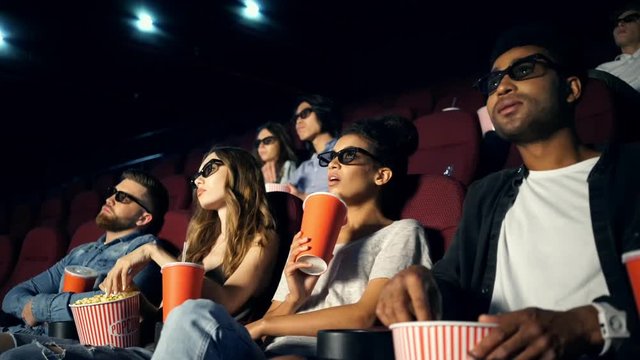 Young bored multiethnic spectators in 3d glasses watching film in cinema