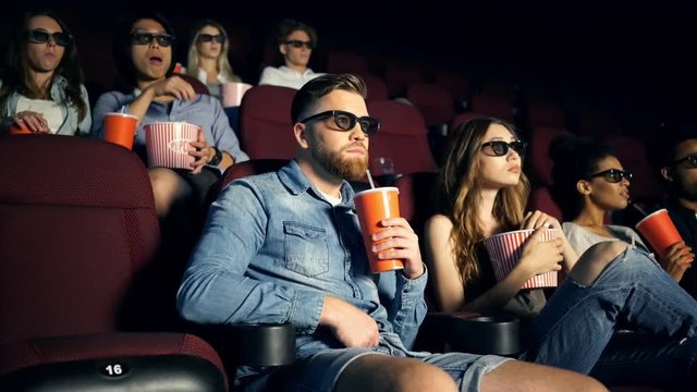 Smiling concentrated spectators watching movie and eating popcorn in cinema
