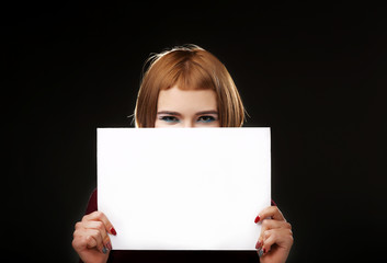 Red-haired woman holding an empty A4 card. Isolated on black background. Space for text