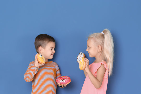 Little children with sweet donuts on color background