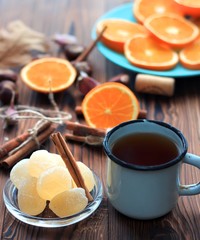 marmalade and a mug of tea with cinnamon on a wooden background. With orange slices in the background.