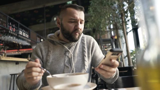 Young man browsing internet on smartphone during meal in cafe
