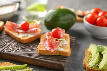 Delicious sandwich with salami and cherry tomato on wooden board