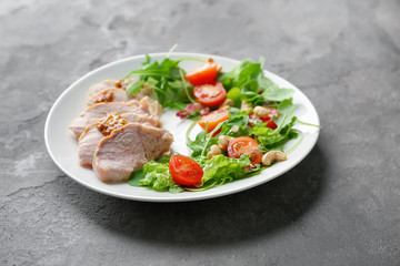 Plate with meat and delicious vegetable salad on grey background