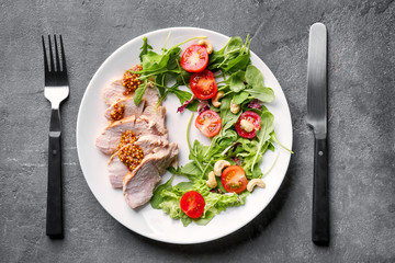 Plate with meat and delicious vegetable salad on grey background, top view