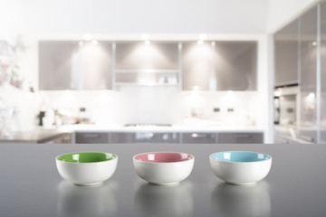 Naklejka na ściany i meble Three colored bowls on steel kitchen top with blur kitchen in the background