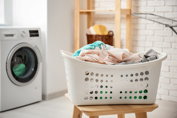 Fototapeta na wymiar Basket with laundry on stool and washing machine in bathroom