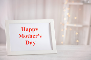 Frame with phrase HAPPY MOTHER'S DAY on table