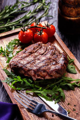 Juicy portions of grilled fillet steak served with tomatoes and roast vegetables on an old wooden board.