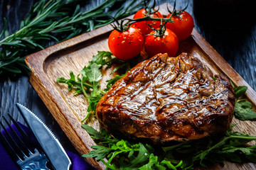 Juicy portions of grilled fillet steak served with tomatoes and roast vegetables on an old wooden board.