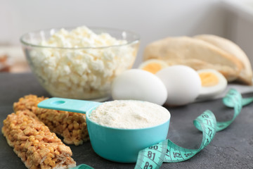 Scoop with protein powder, products and measuring tape on table, closeup
