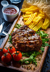 Juicy portions of grilled fillet steak served with tomatoes and roast vegetables on an old wooden board.