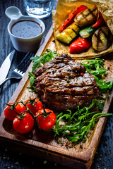 Juicy portions of grilled fillet steak served with tomatoes and roast vegetables on an old wooden board.
