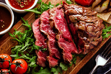 Juicy rare sliced grilled fillet steak served with tomatoes and roast vegetables on an old wooden board.