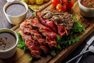 Juicy rare sliced grilled fillet steak served with tomatoes and roast vegetables on an old wooden board.