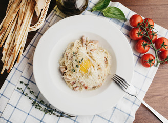 Italian pasta Carbonara with egg yolk in a white plate on a dark wooden table