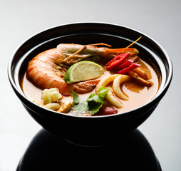 Tom Yam soup with seafood in a black plate.