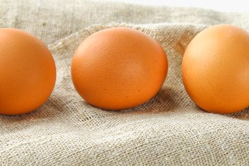 Raw brown chicken eggs in one row on burlap on a white wooden table. Ingredients for cooking.