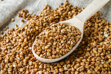 Raw buckwheat in a spoon on sackcloth on a wooden background. Healthy diet food.