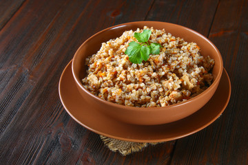 Boiled buckwheat in a bowl with pieces of chicken meat and cilantro on a brown wooden table.