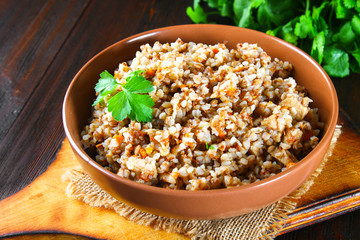 Boiled buckwheat in a bowl with pieces of chicken meat and cilantro on a brown wooden table.