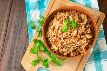 Boiled buckwheat in a bowl with pieces of chicken meat and cilantro on a brown wooden table.
