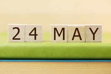 Wooden cube shape calendar for MAY 24 on green book, table. 