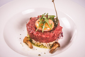 Steak tartare served with egg yolk, onion, pickle, caper, mushroom and rocket salad on a white background