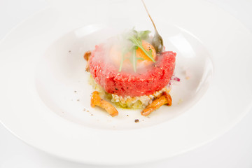 Smoked steak tartare served with egg yolk,  onion, pickle,  caper, mushroom and rocket salad on a white background