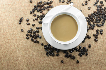 Cup of fresh coffee with coffee beans on burlap warm cup on brown background top view with free space for text