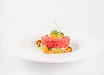 Steak tartare served with egg yolk,  onion, pickle,  caper, mushroom and rocket salad on a white background