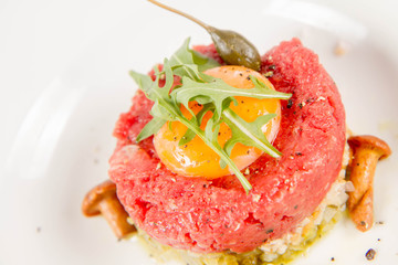 Steak tartare served with egg yolk,  onion, pickle,  caper, mushroom and rocket salad on a white background