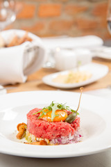 Steak tartare served in a restaurant with egg yolk,  onions, caper, mushroom and rocket salad