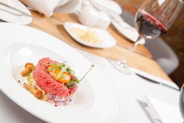 Steak tartare served in a restaurant with egg yolk,  onion, pickles, caper, mushroom and rocket salad