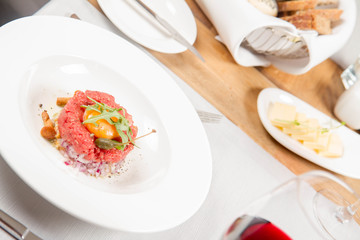 Steak tartare served in a restaurant with egg yolk,  onion, pickles, caper, mushroom and rocket salad