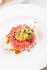 Steak tartare served in a restaurant with egg yolk,  onion, pickles, caper, mushroom and rocket salad