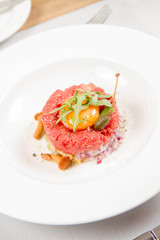 Steak tartare served in a restaurant with egg yolk,  onions, caper, mushroom and rocket salad