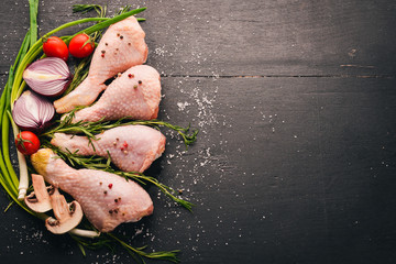 Raw chicken legs with fresh vegetables and rosemary and spices on a black wooden background. Top view. Free space for text.