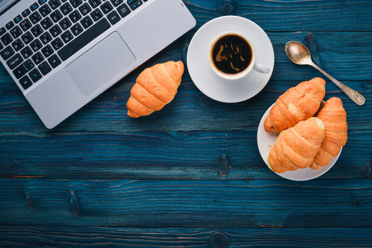 Business breakfast, coffee and croissants, on a wooden surface. Top view. Free space for text.