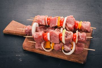 Raw kebab from meat on a wooden background with vegetables. Top view. Free space for text.